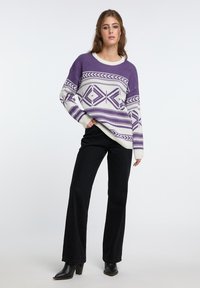 Maglione viola e bianco con motivo, collo rotondo, maniche lunghe e design geometrico. Abbinato a pantaloni neri a campana e stivali neri con tacco.