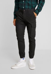 Zwarte cargo joggers met elastische boorden, meerdere zijzakken en een relaxed fit. Het materiaal lijkt lichtgewicht met een zachte textuur.