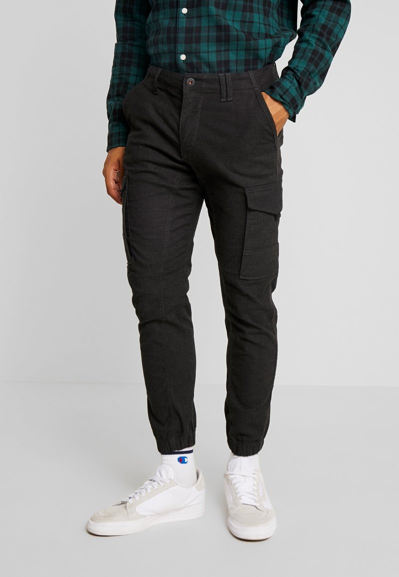 Zwarte cargo joggers met elastische boorden, meerdere zijzakken en een relaxed fit. Het materiaal lijkt lichtgewicht met een zachte textuur.