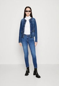 Tamsiai mėlyna džinsinė striukė su sagų užsegimu ir dekoratyvine siuvinėjimu, derinama su šviesiai mėlynais siaurais džinsais ir juodais kulkšnies aulinukais.