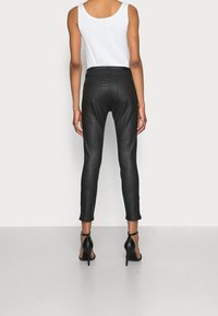 Svarta åtsittande läderbyxor med medelhög midja, avsmalnande ben och synliga sömsdetaljer. Bärs med svarta högklackade skor.