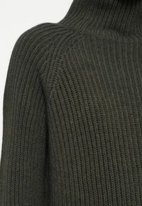 Dunkelgrüner, gerippter Rollkragenpullover mit strukturiertem Strickmuster, hoher Kragen und figurbetontem Schnitt.