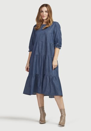 Denim jurk met driekwart pofmouwen, gelaagd ontwerp en midi-lengte. Zachte stof, diepblauwe kleur, gecombineerd met beige enkelschoenen.
