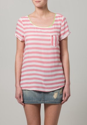 Camicia leggera a strisce rosa e bianche con scollatura arrotondata, maniche corte e taschino frontale; abbinata a una minigonna di denim.