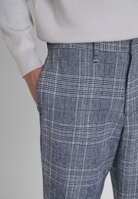 Hose in einem mehrfarbigen blau-weißen karierten Muster, aus strukturiertem Stoff gefertigt; verfügt über Seitentaschen und einen kleinen silberfarbenen Hardware-Akzent.