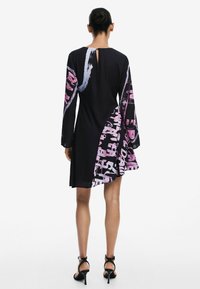 Schwarzes Kleid mit langen Ärmeln; es verfügt über ein grafisches Muster in Pink und Blau auf einer Seite, mit einem Schlüsselloch-Detail im Rücken.