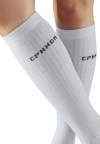 Weiße knielange Socken mit gerippter Textur und schwarzem "CPH"-Schriftzug an der Seite, die am Bündchen eng anliegen.