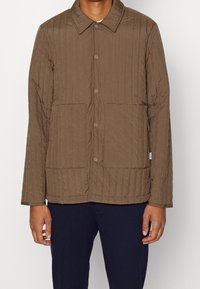 Brun vadderad jacka med krage, knappstängning och två framfickor. Lätt texturerat tyg med vertikal sömnad.