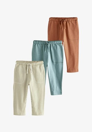 Trzy pary spodni dziecięcych: jedna rdzawa, jedna w kolorze teal, a jedna w paski w odcieniach beżu i brązu. Każda z nich ma elastyczny pas i sznurek do ściągania.