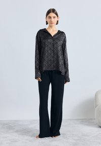 Cămașă neagră cu model, cu guler și nasturi, asortată cu pantaloni negri cu picioare largi. Material neted, cu un luciu subtil și croială lejeră.