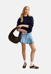 Maglione lavorato a maglia blu marino, gonna plissettata in denim chiaro, borsa a spalla marrone scuro, calzini bianchi alla caviglia e sneaker marroni con accenti bianchi.