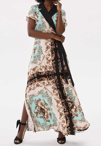 Robe maxi dans une palette de couleurs bleu clair, beige et noir avec des motifs bruns ornés. Comprend un col et une fente sur le côté, fabriquée à partir d'un tissu lisse.