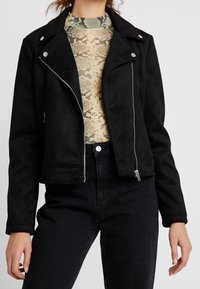 Černá motorkářská bunda z umělé semišové kůže se stříbrným zapínáním na zip vpředu, cvočky a krátkým střihem, doplněná topem se vzorem hadí kůže.