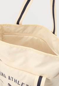 Μπεζ τσάντα tote με λουριά σε στυλ navy με ρίγες. Το εσωτερικό διαθέτει τσέπη με φερμουάρ και λεία, υφή φόδρα. Το λογότυπο PUMA είναι τυπωμένο στο πλάι.