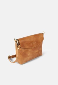 Tasche aus braunem Leder als Crossbody mit Klappenverschluss, goldenen Beschlägen, verstellbarem Riemen und glatter, leicht strukturierter Oberfläche.