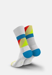 Bunte Socken aus gestricktem Stoff. Sie besitzen geometrische Muster in Rot, Gelb und Blau auf weißem Grund. Die Zehen- und Fersenpartien sind in unitärem Blau akzentuiert.