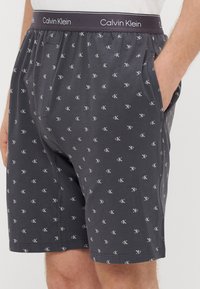 Sive bombažne boksarice Calvin Klein z vzorcem belega logotipa, elastičnim pasom in žepi.