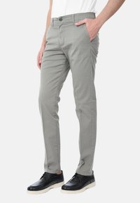 Pantaloni grigi chiari realizzati in tessuto morbido, con vestibilità slim, tasche laterali e chiusura a bottone, abbinati a scarpe nere.