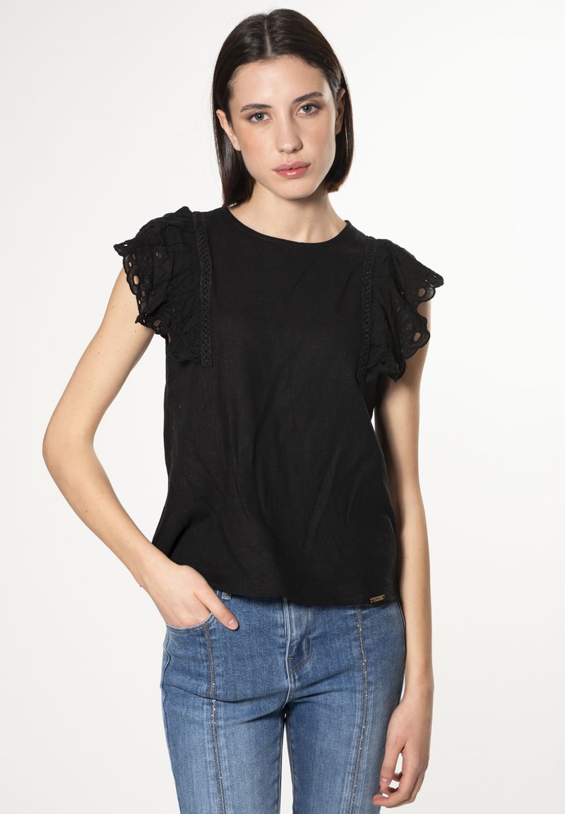 Camicia nera in lino con maniche in pizzo arricciato e dettagli intricati sulle spalle, abbinata a jeans blu aderenti. Design semplice e chic.