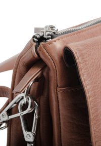 Sac à main en cuir marron avec une surface texturée, doté d'une fermeture éclair et de quincaillerie en métal argenté, ainsi qu'une poche latérale avec un fermoir en métal.