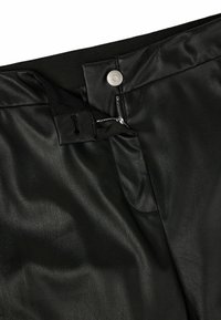 Gros plan sur un pantalon en cuir noir montrant une fermeture éclair partiellement dézippée, un bouton-pression et une ceinture élastique.