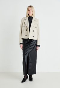 Jachetă bej cropped cu două rânduri de nasturi, bluză neagră din tricot, fustă maxi din piele neagră cu fanta pe față. Pantofi negri cu vârf ascuțit completează look-ul.