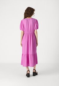 Rosa, lagerad maxiklänning med puffärmar och elastisk midja. Tillverkad av lätt tyg med en krinklad textur. Svarta kraftiga sandaler.