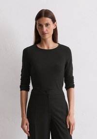 Zwarte lange mouwen top met een ronde halslijn, gemaakt van gladde stof. Gestyled met hoge zwarte broeken. Eenvoudig en aangesloten ontwerp.