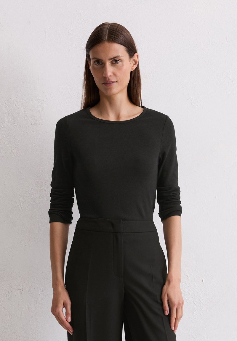 Zwarte lange mouwen top met een ronde halslijn, gemaakt van gladde stof. Gestyled met hoge zwarte broeken. Eenvoudig en aangesloten ontwerp.