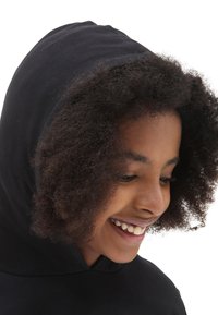 Sudadera negra con una textura suave, que presenta una capucha con cordones. El enfoque está en un niño sonriente con cabello rizado.