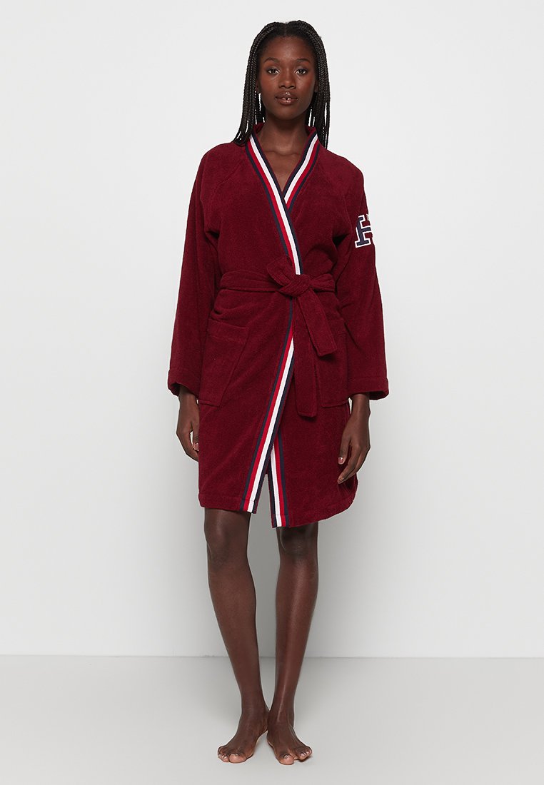 Peignoir bordeaux en tissu éponge doux, avec une ceinture à nouer, des rayures blanches et bleues contrastées, et un logo brodé sur la manche.