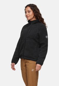 Veste en polaire noire avec fermeture éclair intégrale, col haut, deux poches avant et logo brodé sur la manche gauche. Tissu texturé.