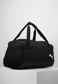 Borsa a duffel nera con tessuto resistente, forma rettangolare, pannello laterale in rete, doppio manico e logo Puma bianco sul fronte.
