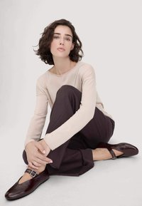 Burgunderfarbene Lederballetschuhe mit einer runden Zehe und einem Knöchelriemen; kombiniert mit einem hellbeigen Langarmshirt und dunklen Hosen; glatte Textur.