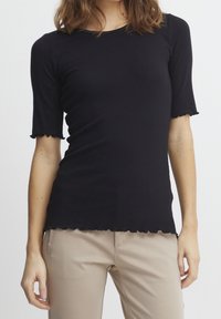 Black ribbed t-shirt with short sleeves and scalloped edges. Lightweight fabric, fitted design, and a rounded neckline.