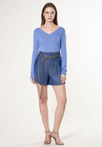 Lichtblauw, lange mouwen V-hals top gecombineerd met hoge taille, gestructureerde denim shorts met een kettingriem, aangevuld met naakte, gescheurde hakken.