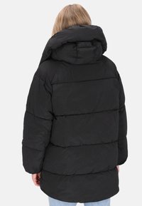 Sort pufferjakke med høj krave, vandret quiltet design og elastiske manchetter. Bagudsigten viser en afslappet pasform og let afrundet nederdel.