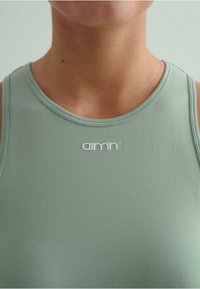 Ljusgrön sporttopp i mjukt tyg. Har rund hals och en liten vit logotyp på bröstet. Minimalistisk design.