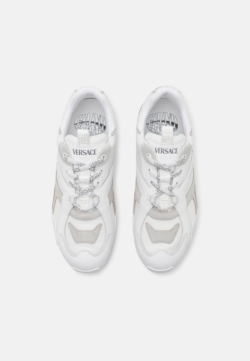 White sneakers with mesh and leather accents. Features a chunky design, gray detailing, lace-up front, and Versace branding on the tongue.