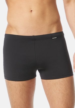 Schwarze Badehose aus dehnbarem Material. Sie haben ein figurbetontes Design, eine mittelhohe Taille und minimalistische Nähtdetails.