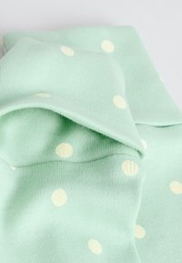 Puha menta zöld szövet fehér pöttyökkel, összehajtva bemutatva, látható kötött textúrával és sima felülettel.