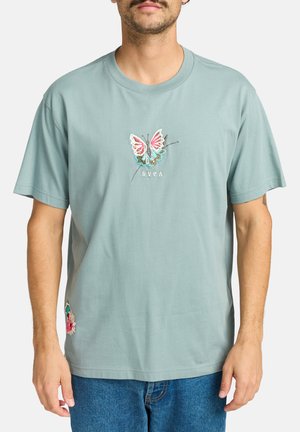 T-shirt in cotone turchese chiaro con design di farfalla ricamato in rosa, blu e nero, e dettagli di ricamo floreale sull'orlo.
