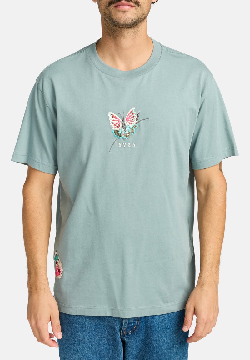 Lys teal bomulds-T-shirt med broderet sommerfugledesign i pink, blå og sort, med blomsterbroderi detalje ved kanten.