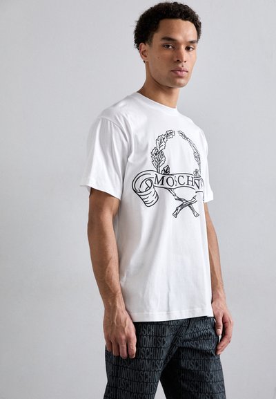 T-shirt en coton blanc avec un imprimé graphique noir de feuilles et un ruban portant le texte "MOSCHINO", à manches courtes, coupe décontractée.
