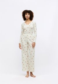 Svetlé loungewear súprava krémovej farby s dlhými rukávmi a širokými nohavicami; obsahuje malé kvetinové vzory a zvlnené okraje.
