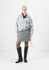 Fleece pullover in blauw en crèmekleurig geometrisch patroon, grijze minirok, doorschijnende zwarte panty, en zwarte kniehoogte hoge haklaarzen. Witte handtas.