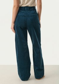 Wijde corduroy broek in donker teal. Kenmerkt zich door verticale ribbels, hoge taille en achterzakken. Glad oppervlak met een lichte glans.
