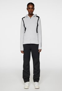 Ljusgrå zip-up huvtröja med svarta detaljer, kängurufickor och dragsko i huvan, ihop med svarta cargo-byxor och vita sneakers.