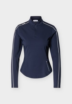 Haut de sport à manches longues bleu marine avec demi-fermeture éclair, passepoil blanc le long des manches et des épaules, et petit logo J.Lindeberg près de l'ourlet.
