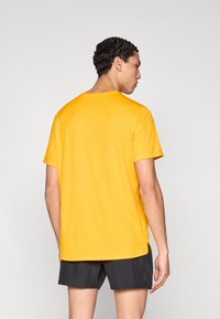 Κίτρινο κοντομάνικο μπλουζάκι από λείο ύφασμα, με στρογγυλή λαιμόκοψη και άνετη εφαρμογή, συνδυασμένο με σκουρόχρωμο σορτς.